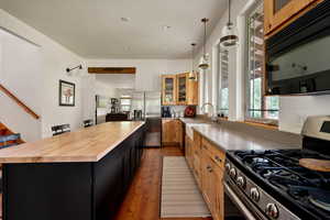 Kitchen featuring appliances with stainless steel finishes, wood counters, a kitchen island, hardwood / wood-style flooring, and glass insert cabinets