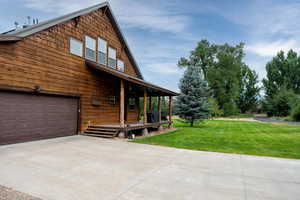 View of side of property featuring a garage, a lawn, driveway, and covered porch