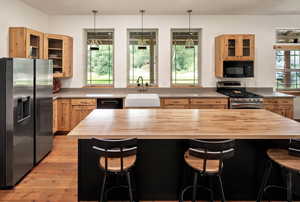 Kitchen with appliances with stainless steel finishes, butcher block counters, glass insert cabinets, and light brown cabinetry