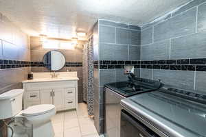 Bathroom with a textured ceiling, independent washer and dryer, tile walls, vanity, and marble look tile flooring