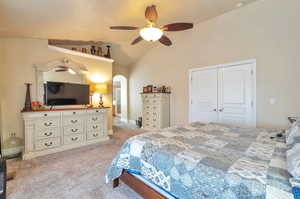 Carpeted bedroom featuring arched walkways, a closet, ceiling fan, and vaulted ceiling