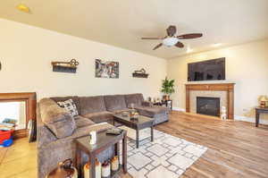 Living room with ceiling fan, a tile fireplace, and wood finished floors