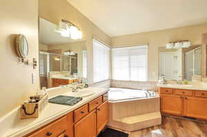 Bathroom featuring a stall shower, two vanities, a garden tub, and wood finished floors