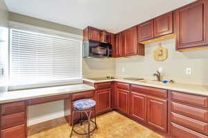 Kitchen featuring black appliances, dark brown cabinets, built in desk, light countertops, and light tile patterned floors