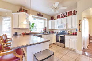 Kitchen with electric range, white microwave, a peninsula, and white cabinets