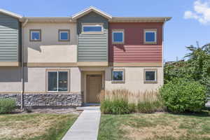 Townhome / multi-family property with stucco siding, a front lawn, and stone siding