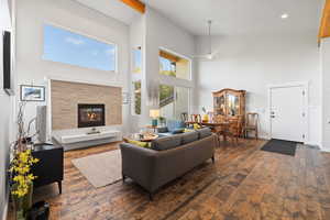 Living area featuring a high ceiling, dark wood-style floors, a stone fireplace, and recessed lighting