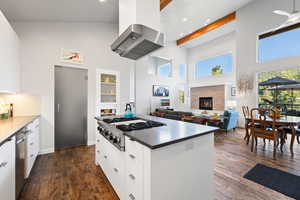 Kitchen with appliances with stainless steel finishes, wall chimney range hood, high vaulted ceiling, modern cabinets, and white cabinetry