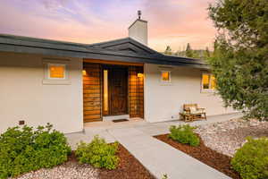 Exterior entry at dusk with stucco siding and a chimney