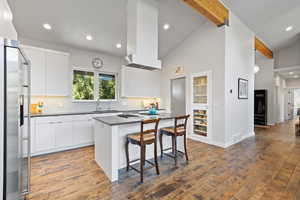 Kitchen featuring stainless steel appliances, modern cabinets, a center island, dark countertops, and beam ceiling