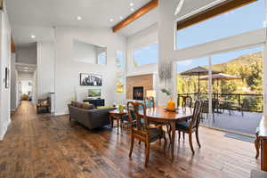 Dining space with hardwood / wood-style flooring, a glass covered fireplace, high vaulted ceiling, beamed ceiling, and recessed lighting