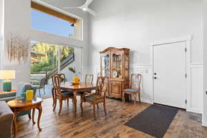Dining area featuring a towering ceiling, dark wood finished floors, a wainscoted wall, ceiling fan, and a decorative wall