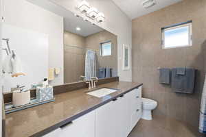 Bathroom featuring vanity, tile walls, tile patterned flooring, a tile shower, and plenty of natural light