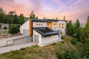 Back of house at dusk featuring roof mounted solar panels, stucco siding, driveway, a balcony, and an attached garage