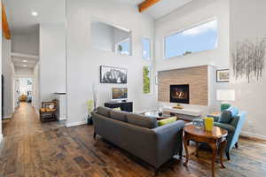 Living area featuring dark wood-style floors, beamed ceiling, a stone fireplace, high vaulted ceiling, and recessed lighting
