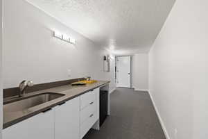 Kitchen featuring a textured ceiling, white cabinetry, dark countertops, and dark colored carpet