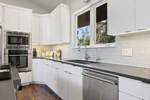 Kitchen featuring stainless steel appliances, dark wood-type flooring, lofted ceiling, white cabinetry, and dark countertops