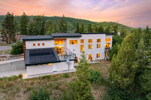 Back of property at dusk featuring roof mounted solar panels, a balcony, stucco siding, a wooded view, and a mountain view