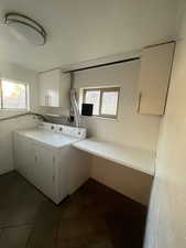 Washroom featuring cabinet space, washing machine and clothes dryer, healthy amount of natural light, and dark tile patterned flooring