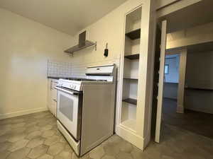 Kitchen featuring white range with gas stovetop, open shelves, built in features, and light tile patterned flooring
