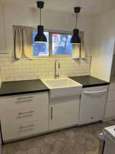Kitchen with dishwasher, white cabinets, dark countertops, and decorative light fixtures