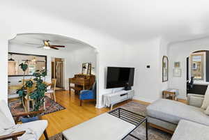 Living room featuring arched walkways, ceiling fan, wood finished floors, and healthy amount of natural light