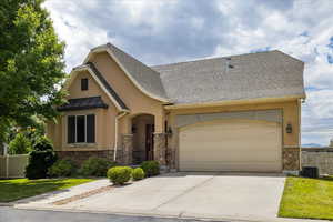 View of front facade featuring stone siding, stucco siding, an attached garage, concrete driveway, and a standing seam roof