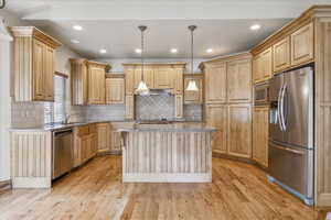 Kitchen featuring appliances with stainless steel finishes, light stone counters, ventilation hood, light wood-style flooring, and light brown cabinetry