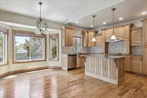 Kitchen featuring dishwasher, light wood-style flooring, decorative backsplash, light stone counters, and lofted ceiling