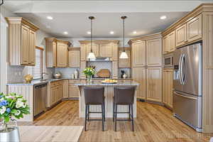 Kitchen with stainless steel appliances, light wood-style floors, a center island, light stone counters, and a kitchen breakfast bar