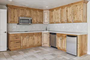 Kitchen with stainless steel appliances, tasteful backsplash, tile countertops, recessed lighting, and light stone finish flooring