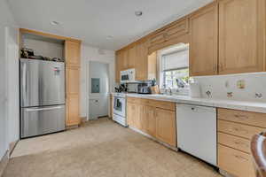 Kitchen featuring white appliances, light brown cabinets, electric panel, decorative backsplash, and light flooring