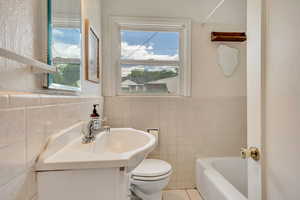 Full bath featuring tile walls, vanity, a bath, plenty of natural light, and wainscoting