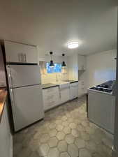 Kitchen featuring white appliances, white cabinets, decorative backsplash, and pendant lighting