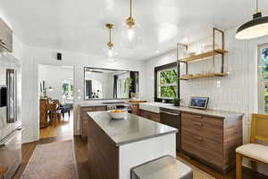 Kitchen featuring modern cabinets, stainless steel appliances, brown cabinetry, a center island, and dark wood-style flooring