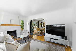 Living area featuring arched walkways, wood finished floors, a brick fireplace, and ceiling fan