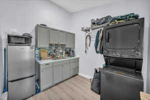 Laundry area featuring stacked washer / drying machine and light wood finished floors