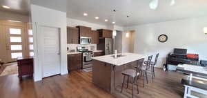 Kitchen featuring stainless steel appliances, a breakfast bar area, dark wood finished floors, an island with sink, and light countertops