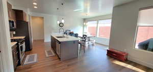 Kitchen featuring appliances with stainless steel finishes, dark wood-style flooring, an island with sink, a kitchen breakfast bar, and light countertops