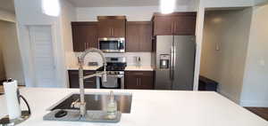 Kitchen with appliances with stainless steel finishes, light countertops, dark brown cabinets, backsplash, and pendant lighting