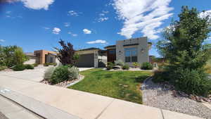 View of front of property featuring driveway, stucco siding, an attached garage, and a front yard Summer 2025