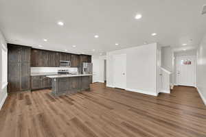 Kitchen featuring appliances with stainless steel finishes, recessed lighting, a kitchen island with sink, light countertops, and wood finished floors