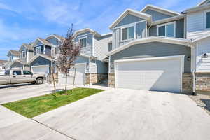 View of front facade with an attached garage, board and batten siding, driveway, stone siding, and a residential view