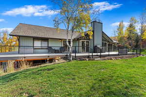 Back of house with a lawn, a chimney, a deck, and roof with shingles