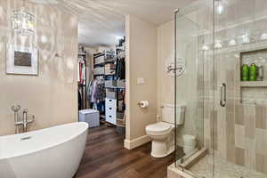 En Suite Primary Bath. Full bathroom with a soaking tub, a stall shower, a walk in closet, wood finished floors, and a textured ceiling