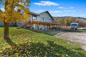 Apartment entrance and driveway. View of front of home with stairs, a deck with mountain view, a front yard, and gravel driveway