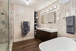 En Suite Primary Bathroom with a soaking tub, a shower stall, wood finished floors, and double vanity