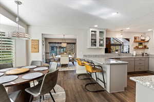 Eat in Kitchen with a textured ceiling, glass insert cabinets, dark wood-style flooring, a peninsula, and pendant lighting