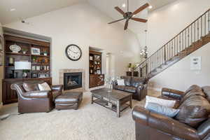Living room with high vaulted ceiling, stairs, ceiling fan, arched walkways, and a tile fireplace