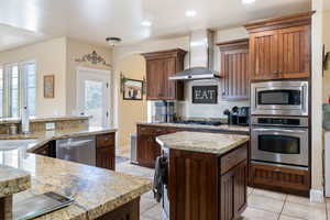 Kitchen with appliances with stainless steel finishes, wall chimney exhaust hood, light tile patterned floors, a center island, and recessed lighting